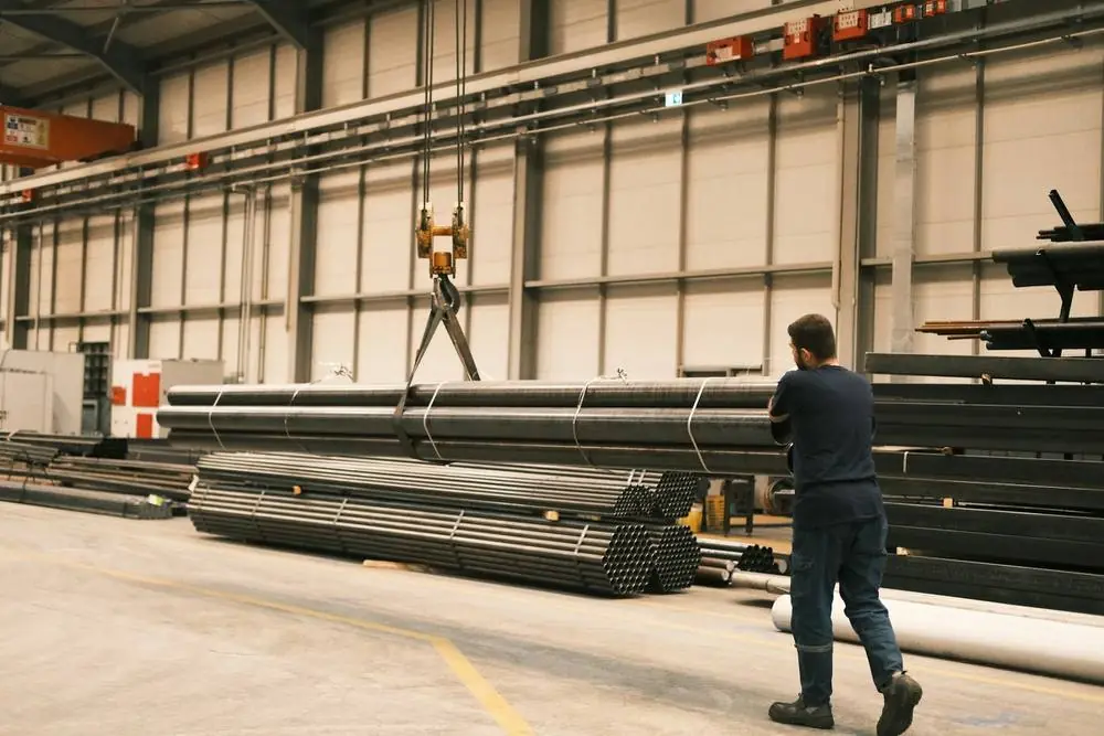 Overhead crane lifting bundled steel pipes inside a warehouse